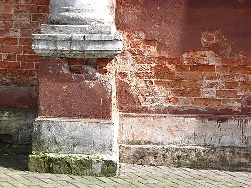 Отслоение штукатурки на фасаде около фундамента, видна засоленная кирпичная кладка