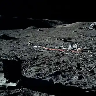 Приборы ALSEP. На переднем плане слева — радиоизотопный термоэлектрогенератор. Левее центра — прибор, регистрирующий частоту падения метеоритов. Правее центра — куча мусора из упаковок. У правого края снимка и чуть выше центра — геофонный модуль. Выше него — скала Geophone Rock. Левее неё — красный флажок в месте размещения одного из геофонов