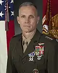 A color image of Glenn Walters, a white male in his Marine Corps Service A uniform. He is not wearing a hat, ribbons are visible. The Marine Corps flag and United States flag are visible in the background.