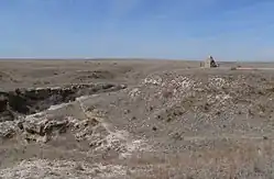 Dry grassland with a small rocky canyon; pyramidal stone monument on hill nearby