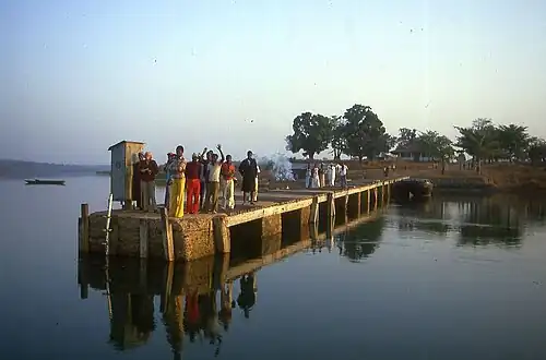 Photographie couleur d'un ponton en béton et en bois, vu depuis un bateau, et sur lequel se tiennent une vingtaine de personnes.