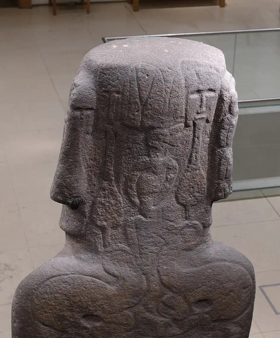 Резьба, идентифицирующая мужчину (слева) и женщину (справа), с их оперением выше, как это предлагается в спорной интерпретации. Также на фотографии видны два больших более ранних komari, которые распространяются на верхнюю часть головы статуи.