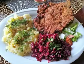 Свиная отбивная, картофельное пюре с укропом и два салата на белой тарелке