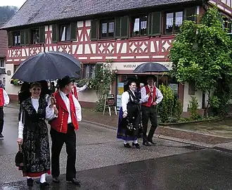 Жители в народных костюмах, на заднем плане — дом XVIII в.