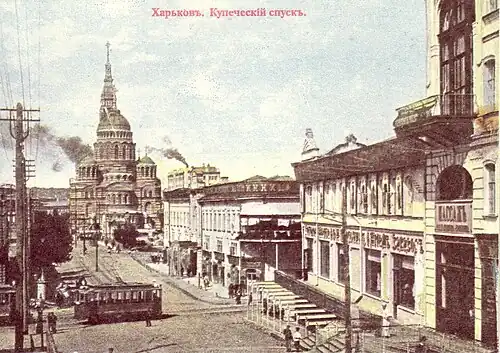 Вид с Купеческого спуска в сторону Купеческого моста, Благовещенской площади и Благовещенского собора. Трамвай едет по улице Клочковской. Справа перед ним расположено здание Старого Пассажа. За Клочковской перед мостом застроены обе стороны улицы.