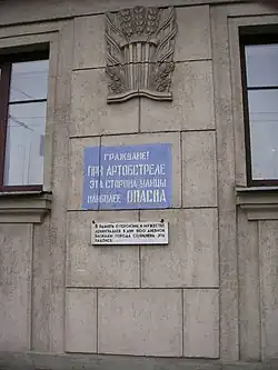 Мемориальная надпись «Граждане! При артобстреле эта сторона улицы наиболее опасна» с памятной доской при ней и полочкой для цветов