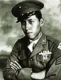 Head and shoulders of a young man wearing a peaked cap and a military jacket with ribbon bars and a badge on the left breast.