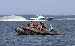 Военнослужащие пограничных органов ФСБ России задерживают лодку условных нарушителей государственной границы на учениях в районе пограничного пункта «Мамоново».На заднем плане: пограничный сторожевой катер ПСКА-306 проекта 12200 из состава ПУ ФСБ России по Калининградской области (2011 год).