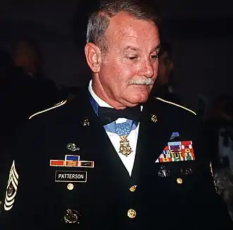 A gray-haired white man wearing a formal military uniform with a star-shaped medal hanging from a ribbon around his neck