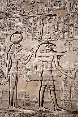 Богиня Менхит стоит слева от Хнума. Барельеф на внешней стене храма в Эсне