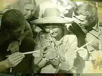 Элеонора Савельева и студенты изучают находку - деревянную чашу