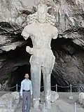 Охранник пещеры рядом со статуей Шапура. Размеры статуи на этой картине вполне узнаваемы по сравнению с человеком, стоящим рядом с ней.