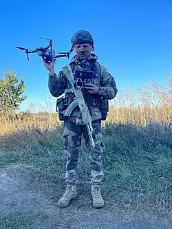 Военнослужащий с квадрокоптером Mavic 2 Pro с закреплённым осколочным боеприпасом в качестве дрона-наблюдателя и дрона-сбросника